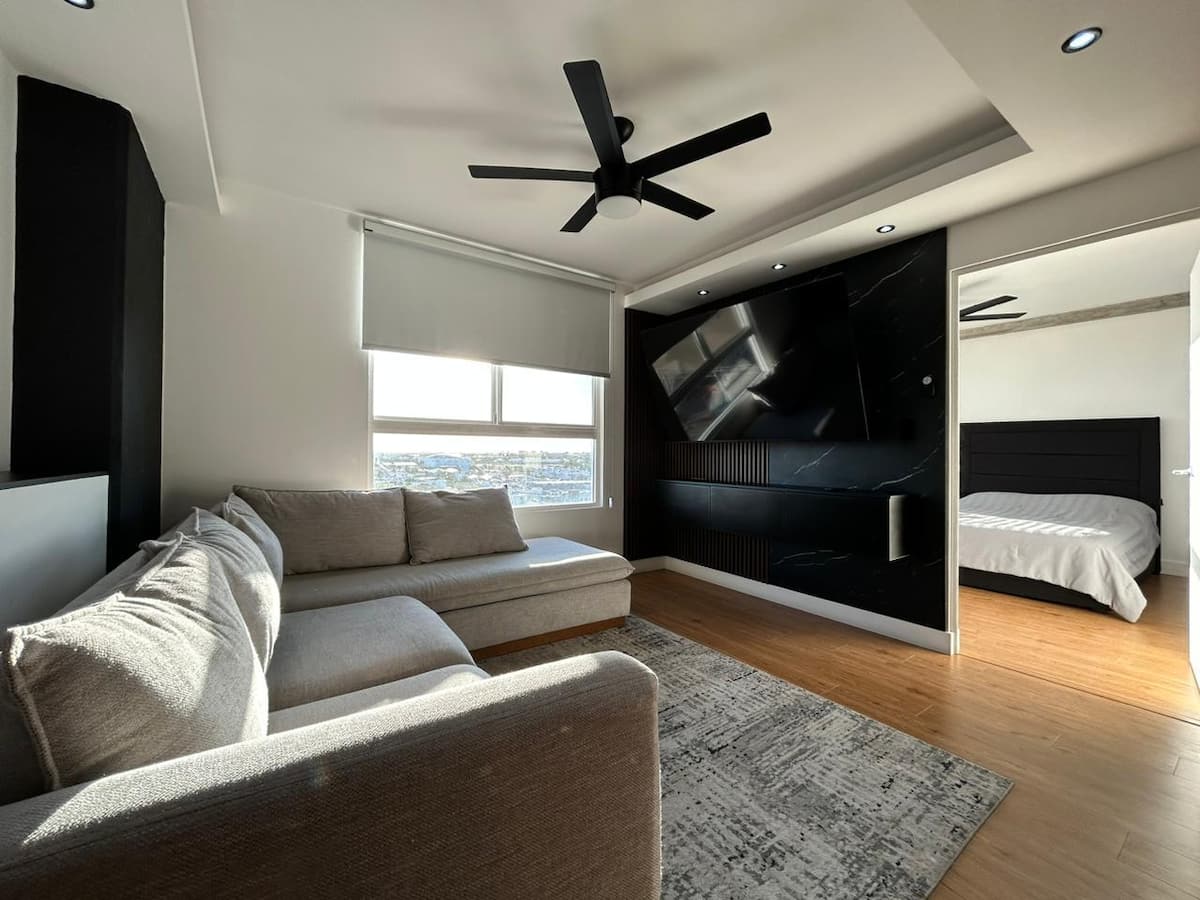 Sala del departamento Hexus 716 en Hermosillo con vista a la ciudad, sofá gris y pantalla en muro negro